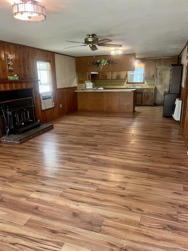unfurnished living room with ceiling fan, a fireplace, wood finished floors, wooden walls, and heating unit