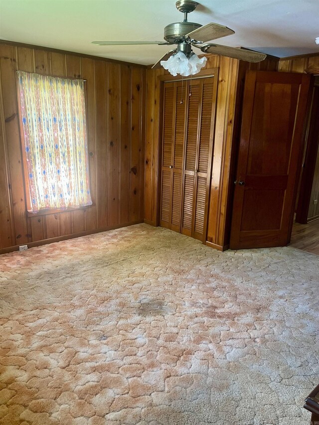 unfurnished bedroom with wood walls, a ceiling fan, and carpet flooring