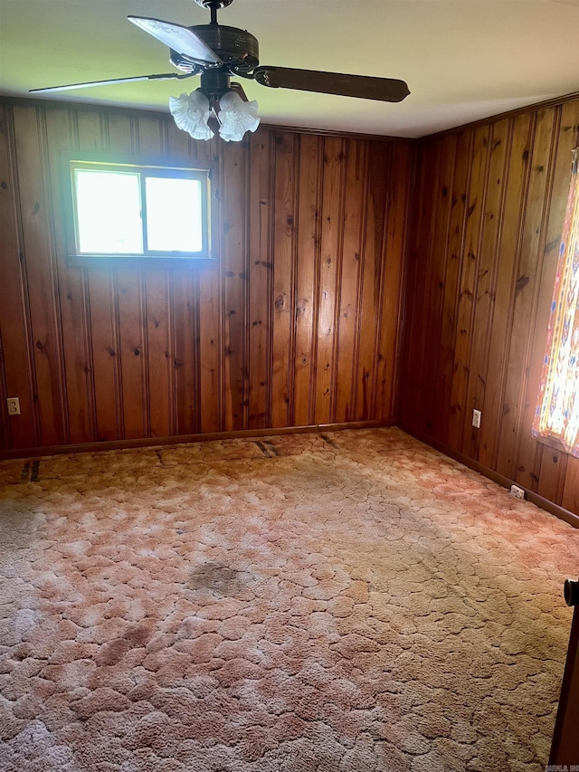 spare room with wooden walls, carpet flooring, baseboards, and a ceiling fan