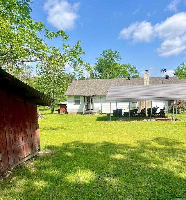 rear view of house featuring entry steps, a yard, a shingled roof, and a chimney