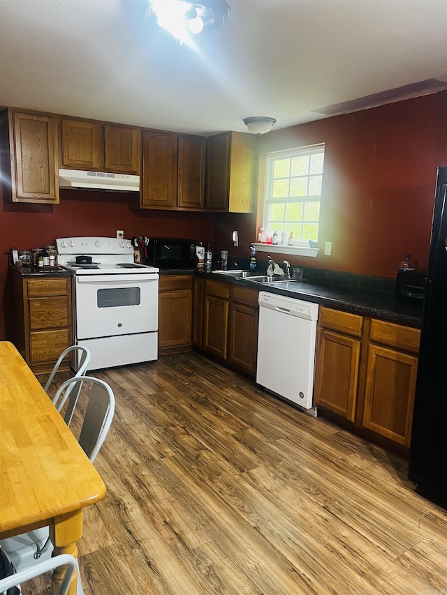 kitchen featuring dark wood-style flooring, dark countertops, brown cabinets, under cabinet range hood, and black appliances