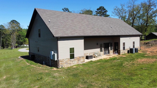 back of house featuring cooling unit, a lawn, a patio, stone siding, and a shingled roof