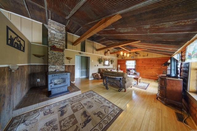 living room featuring wood walls, a wood stove, wood-type flooring, and lofted ceiling with beams
