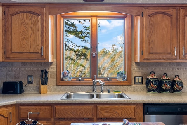 kitchen with light countertops, backsplash, brown cabinets, dishwasher, and a sink