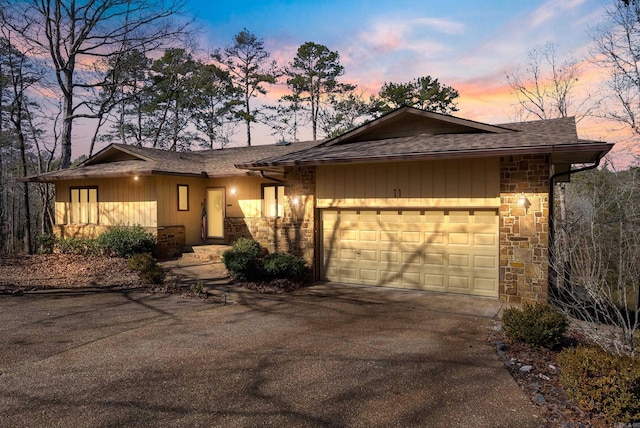 view of front of property featuring aphalt driveway, roof with shingles, stone siding, and an attached garage