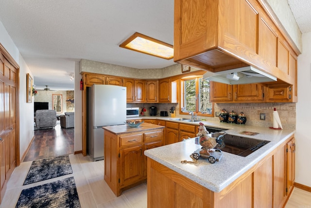 kitchen with tasteful backsplash, a sink, freestanding refrigerator, a peninsula, and white microwave