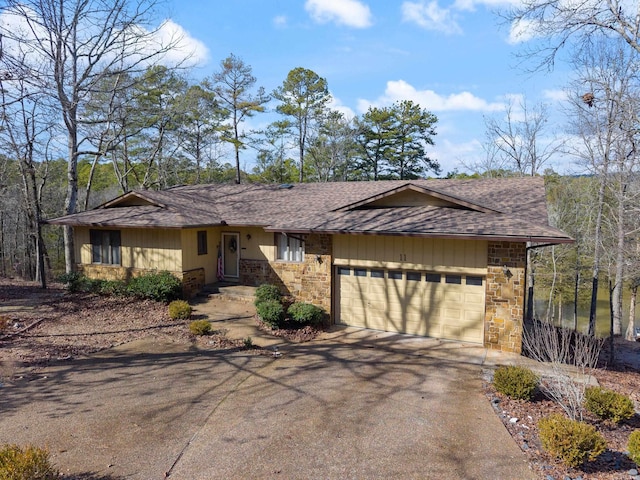view of front facade featuring roof with shingles, driveway, a garage, and stone siding