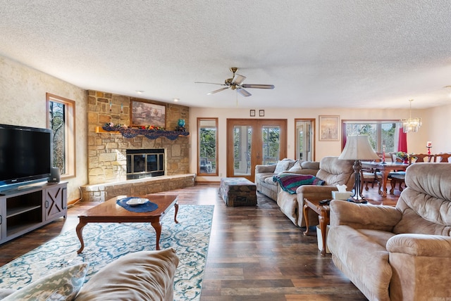 living room featuring dark wood-type flooring, a stone fireplace, a textured ceiling, and ceiling fan with notable chandelier