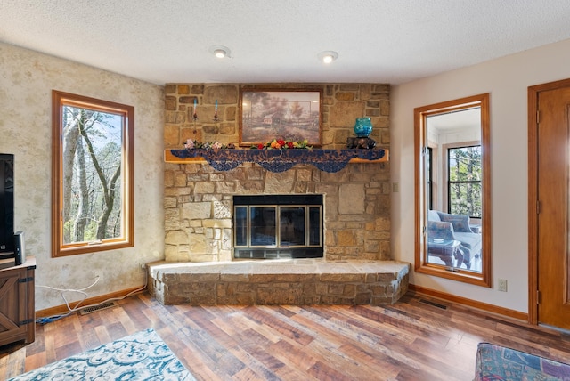 unfurnished living room with visible vents, baseboards, a fireplace, a textured ceiling, and wood finished floors