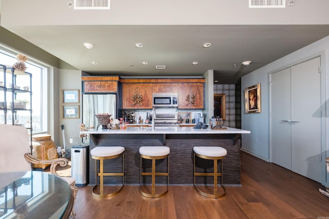 kitchen with visible vents, light countertops, brown cabinetry, stainless steel appliances, and dark wood-type flooring