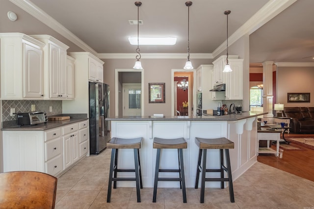 kitchen featuring refrigerator with ice dispenser, dark countertops, a peninsula, and under cabinet range hood