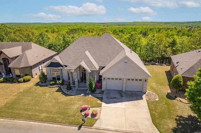 view of front of home with a front yard, stone siding, an attached garage, a wooded view, and driveway