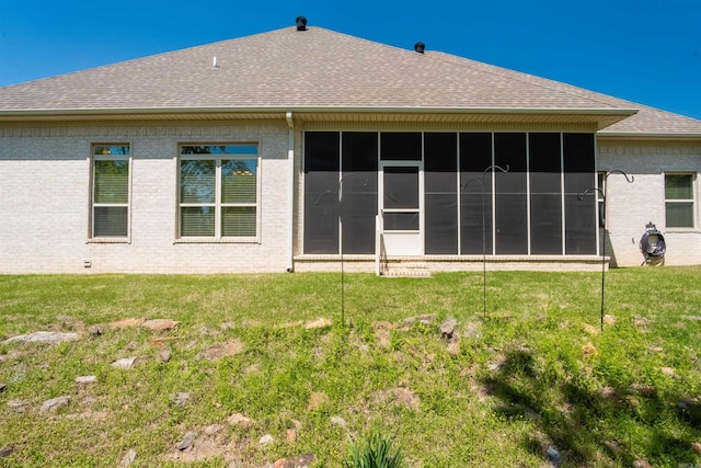 back of property with brick siding, a shingled roof, a sunroom, and a lawn