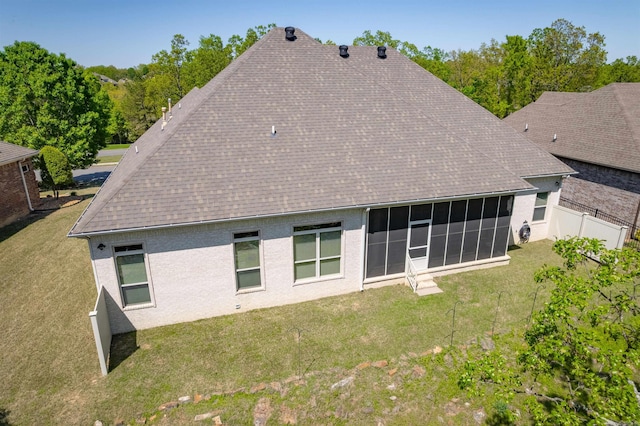 back of property with fence, roof with shingles, a sunroom, and a lawn
