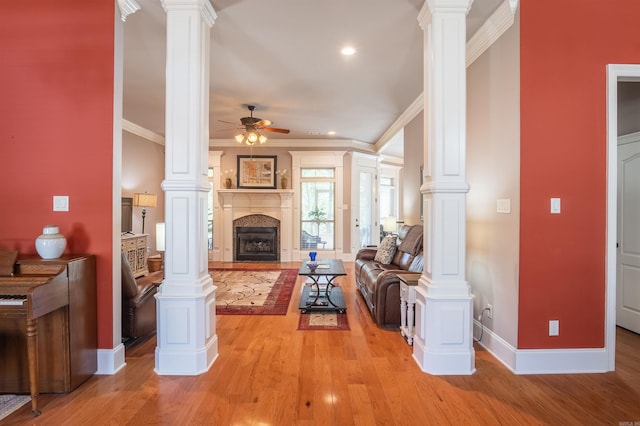 living area featuring decorative columns, light wood-style floors, baseboards, and ceiling fan