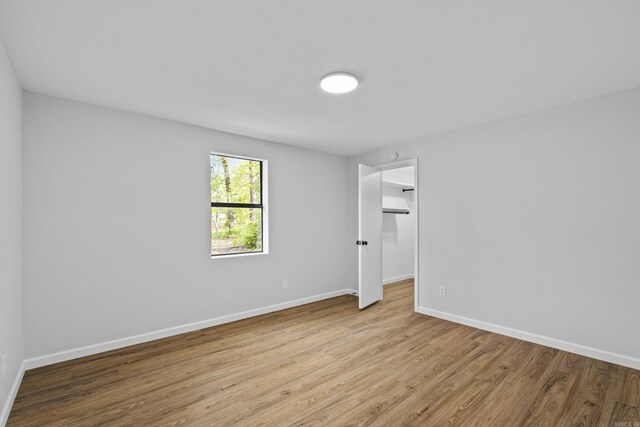 unfurnished bedroom featuring a spacious closet, a closet, baseboards, and wood finished floors