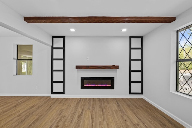 unfurnished living room with a glass covered fireplace, recessed lighting, wood finished floors, baseboards, and beam ceiling