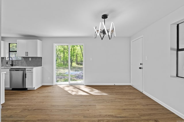 unfurnished dining area featuring light wood-style floors, a notable chandelier, baseboards, and a sink