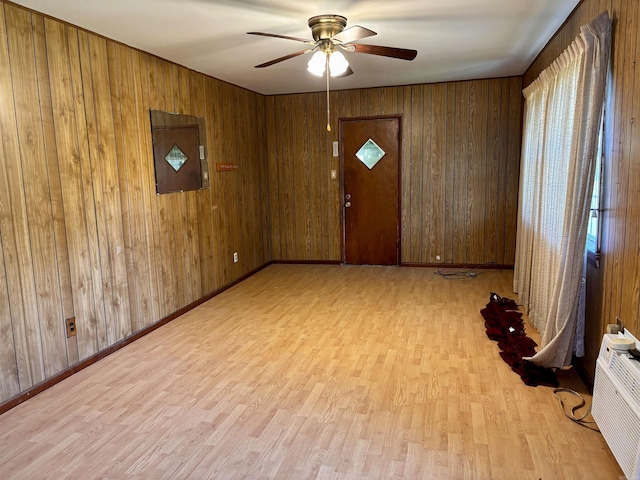spare room with wooden walls, baseboards, light wood finished floors, and a ceiling fan