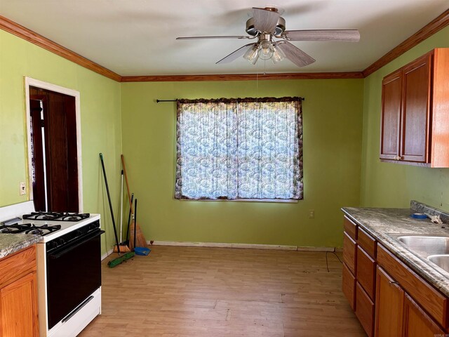 kitchen featuring gas stove, light wood-style flooring, a ceiling fan, crown molding, and a sink
