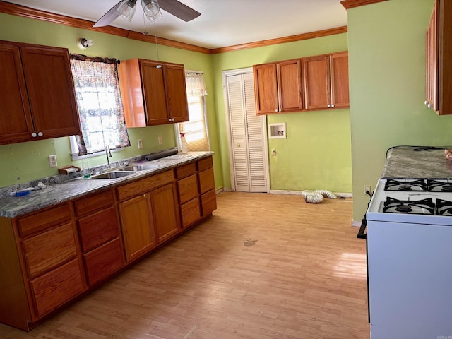 kitchen with light wood-style floors, ceiling fan, ornamental molding, gas range gas stove, and a sink