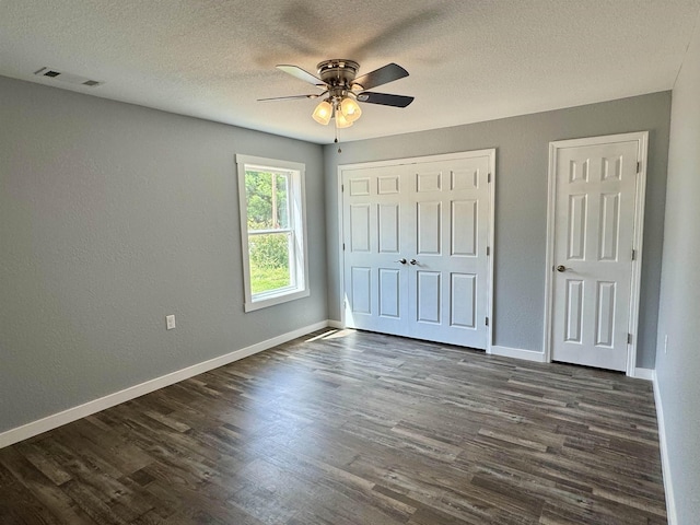unfurnished bedroom with a textured ceiling, a closet, visible vents, baseboards, and dark wood-style floors