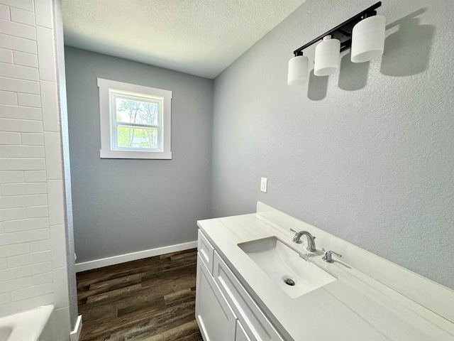 full bath featuring baseboards, a textured wall, a textured ceiling, vanity, and wood finished floors