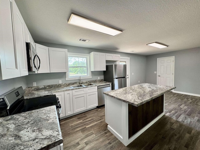 kitchen with dark wood finished floors, white cabinets, a center island, a sink, and stainless steel appliances