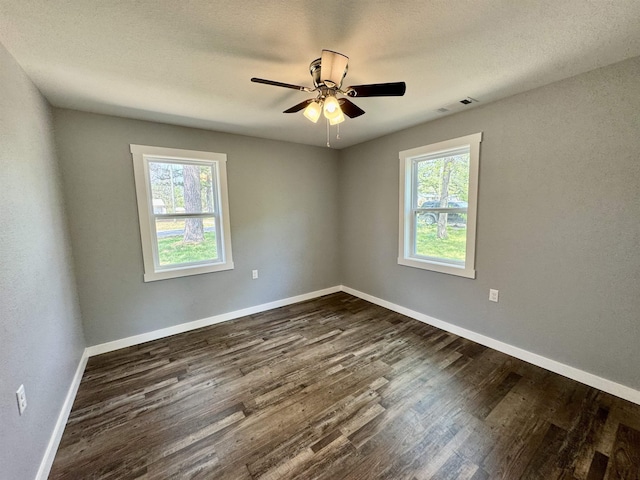 unfurnished room with a wealth of natural light, dark wood-style floors, baseboards, and visible vents