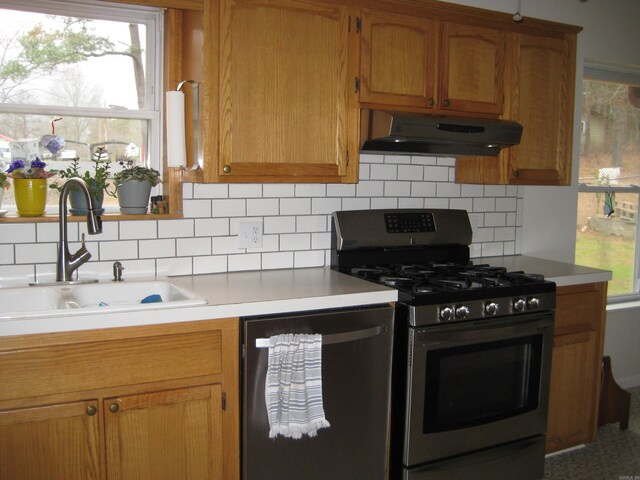 kitchen featuring under cabinet range hood, stainless steel gas range oven, light countertops, dishwasher, and a sink