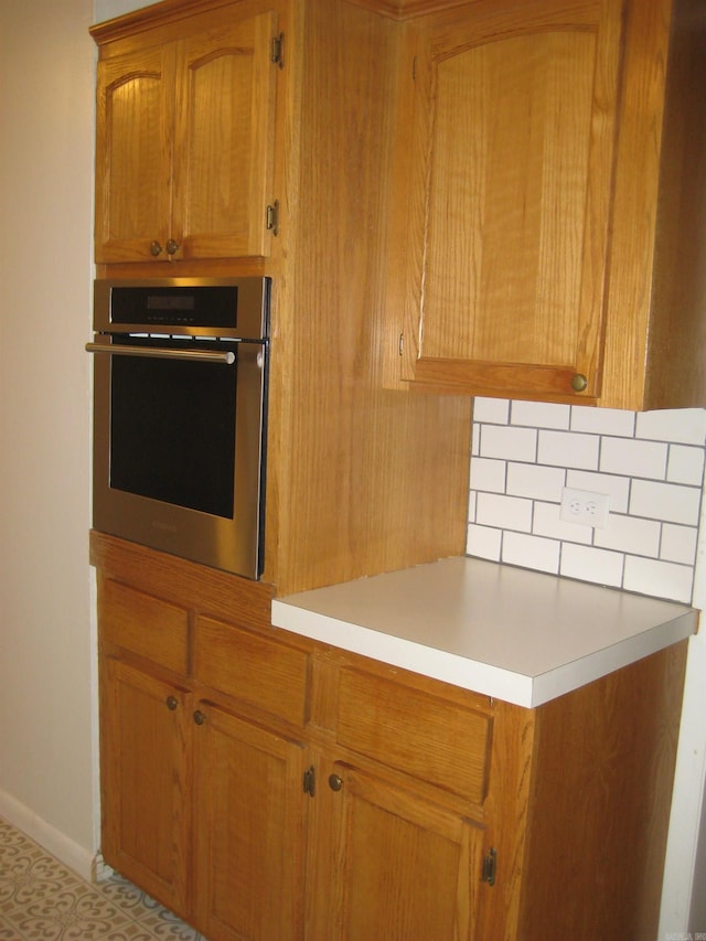 kitchen featuring stainless steel oven, light countertops, baseboards, and brown cabinets