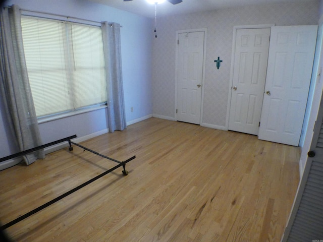 unfurnished bedroom featuring baseboards, multiple closets, and wood finished floors