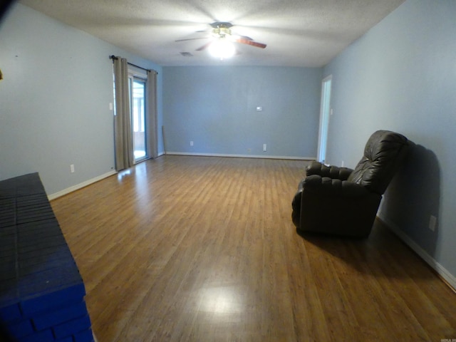 living area with wood finished floors, a ceiling fan, and baseboards