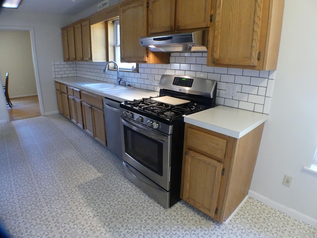 kitchen featuring a sink, decorative backsplash, appliances with stainless steel finishes, light countertops, and under cabinet range hood