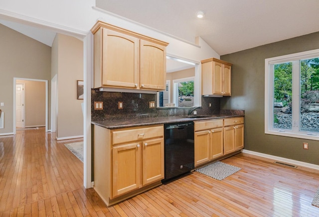 kitchen with lofted ceiling, a sink, black dishwasher, and tasteful backsplash