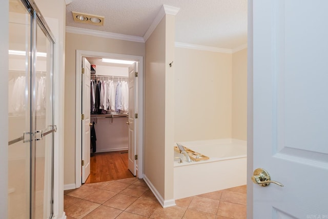 hallway with baseboards, a textured ceiling, light tile patterned floors, and crown molding