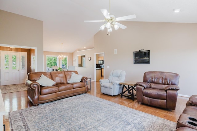 living area featuring high vaulted ceiling, baseboards, ceiling fan with notable chandelier, and light wood-style flooring