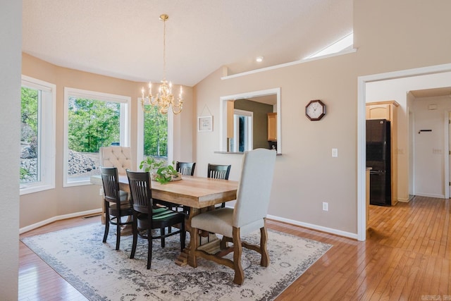 dining room with vaulted ceiling, a healthy amount of sunlight, light wood-type flooring, and an inviting chandelier