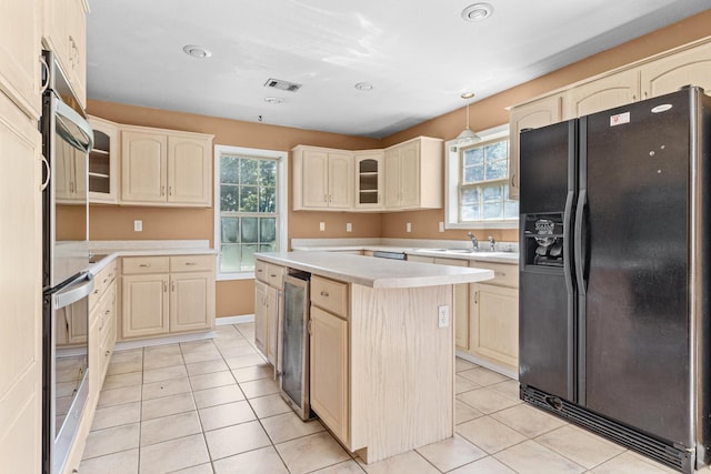kitchen featuring black fridge with ice dispenser, glass insert cabinets, light countertops, visible vents, and a kitchen island
