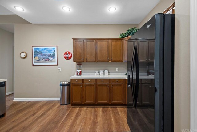 kitchen with light countertops, wood finished floors, freestanding refrigerator, baseboards, and brown cabinetry