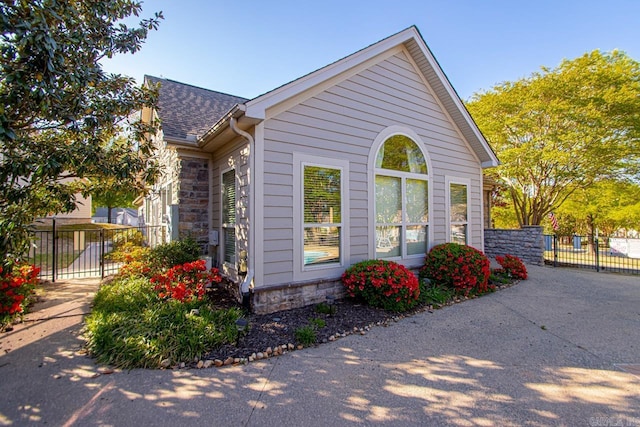 view of home's exterior with stone siding, fence, and a shingled roof