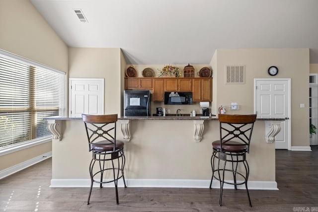 kitchen with brown cabinetry, visible vents, a breakfast bar area, and black appliances