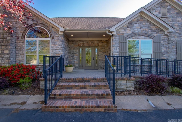 entrance to property with roof with shingles, stone siding, and covered porch