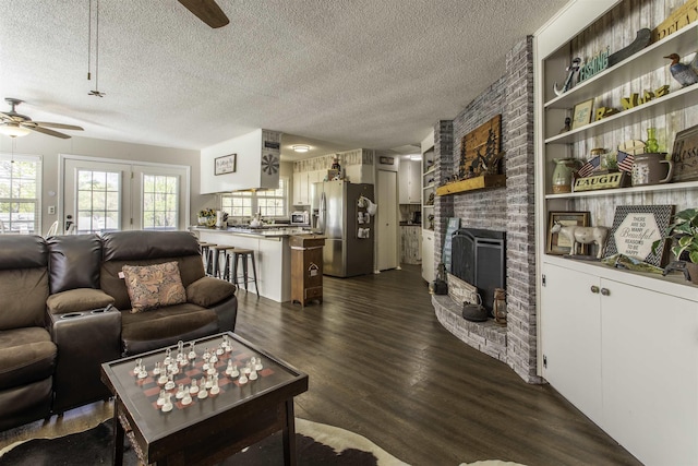 living area featuring a brick fireplace, dark wood-style floors, a textured ceiling, and ceiling fan