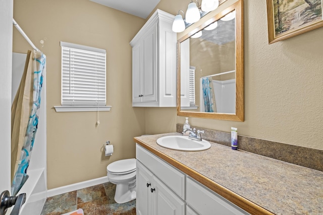 full bath featuring stone finish floor, toilet, vanity, baseboards, and shower / tub combo