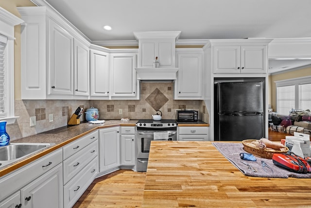 kitchen featuring wooden counters, electric range, white cabinets, backsplash, and freestanding refrigerator