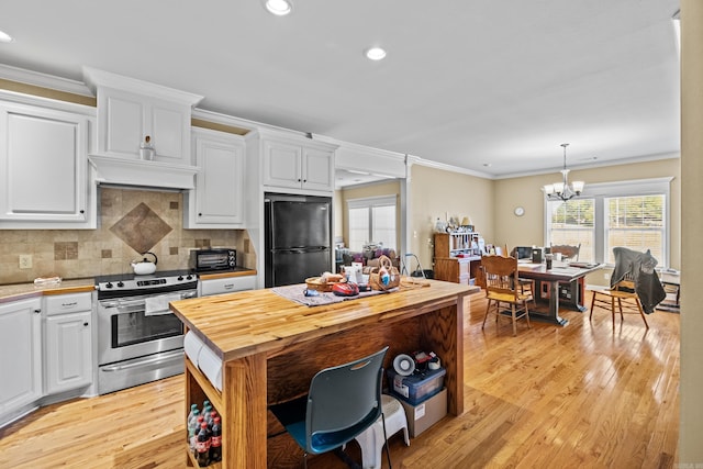 kitchen with white cabinets, stainless steel range with electric cooktop, freestanding refrigerator, butcher block counters, and a notable chandelier
