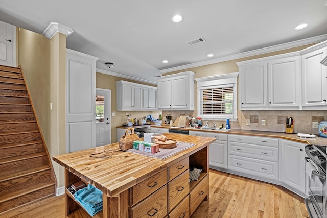 kitchen featuring butcher block countertops, stainless steel range with gas stovetop, white cabinetry, ornamental molding, and visible vents