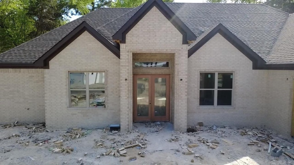 doorway to property featuring brick siding, french doors, and roof with shingles