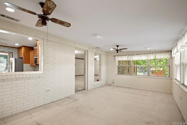 unfurnished living room with ceiling fan, light carpet, brick wall, and visible vents